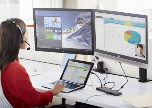 Woman sitting on desk working with laptop looking at a monitor